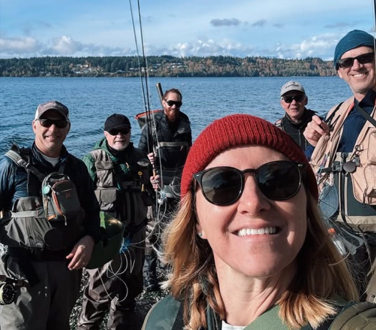 Club members on the shoreline with a smiling member in a red beanie in the foreground